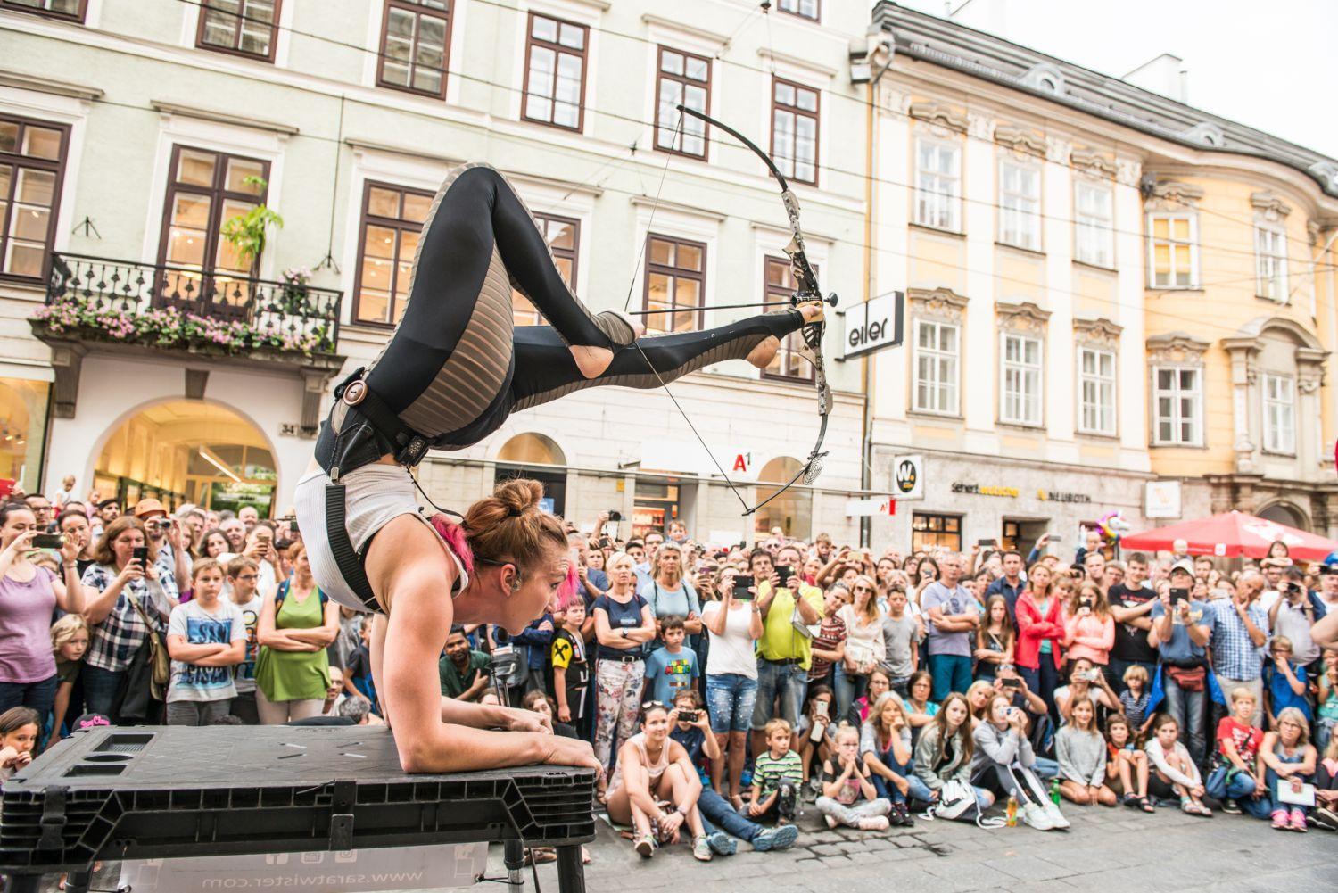 Akrobatik Sara Twister balanciert Pfeil und Bogen auf ihren Füßen