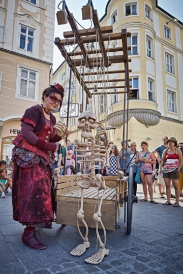 Frau steht neben einem Wagen, an dem eine Skelett-Figur hängt